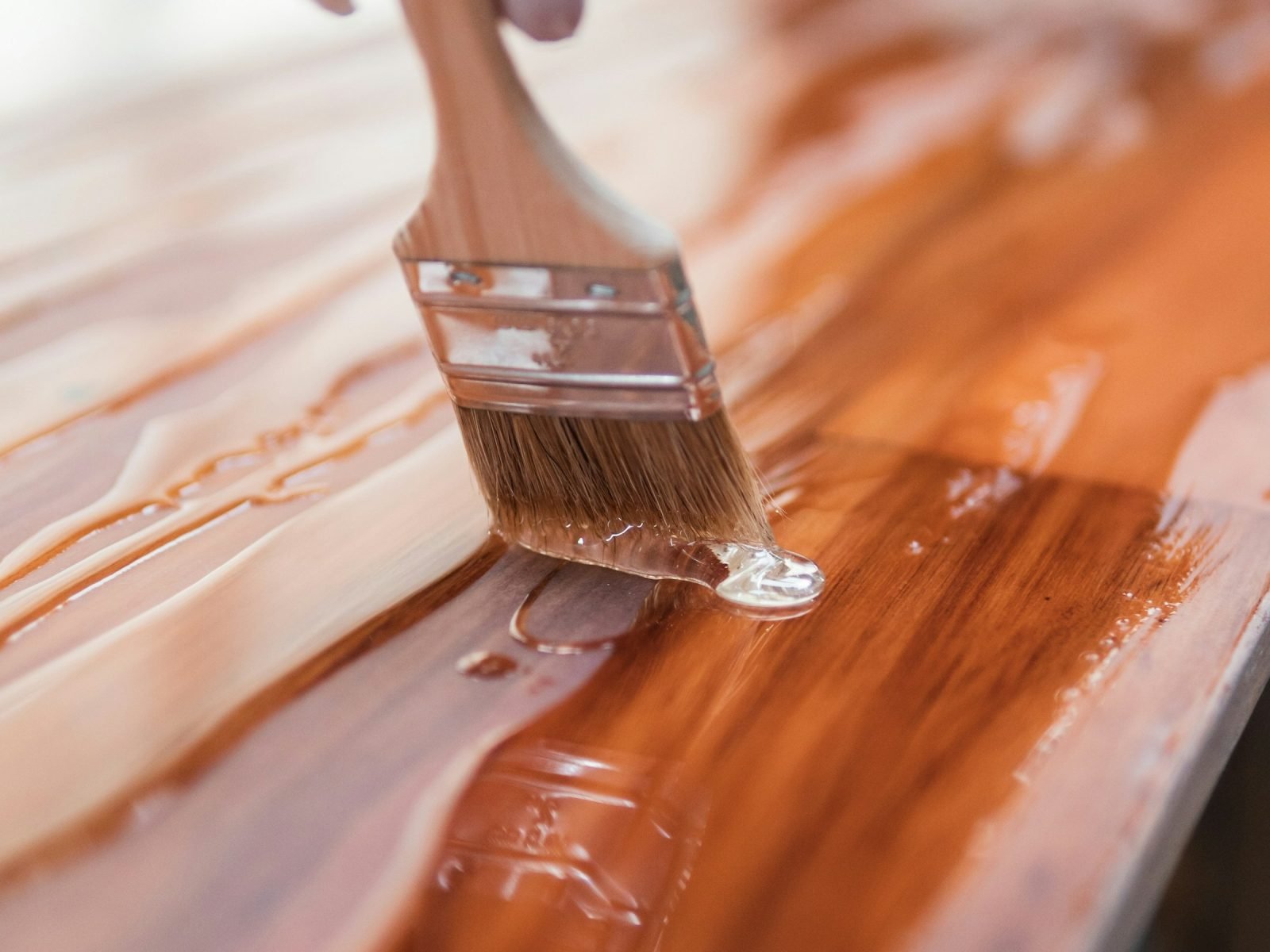 Brush applying a rich wood stain along a timber board