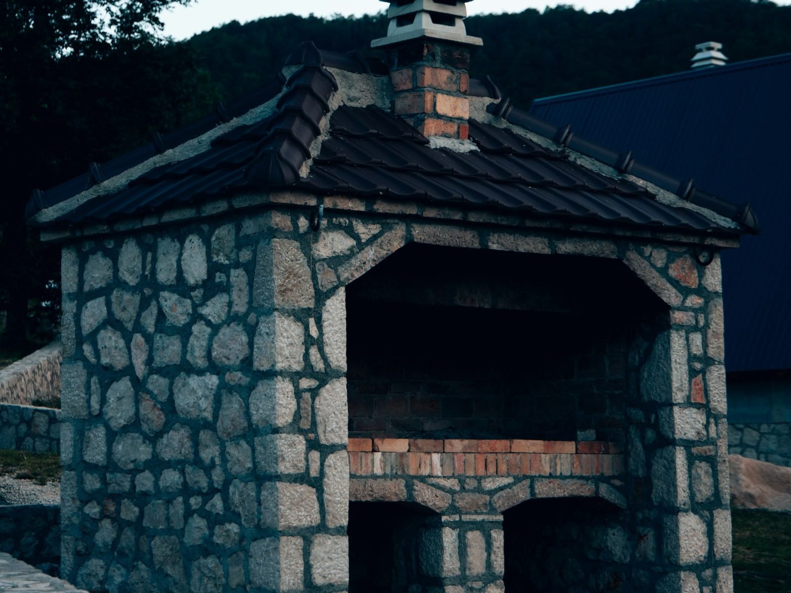 Built-in stone outdoor cooker with a brick chimney and tiled roof
