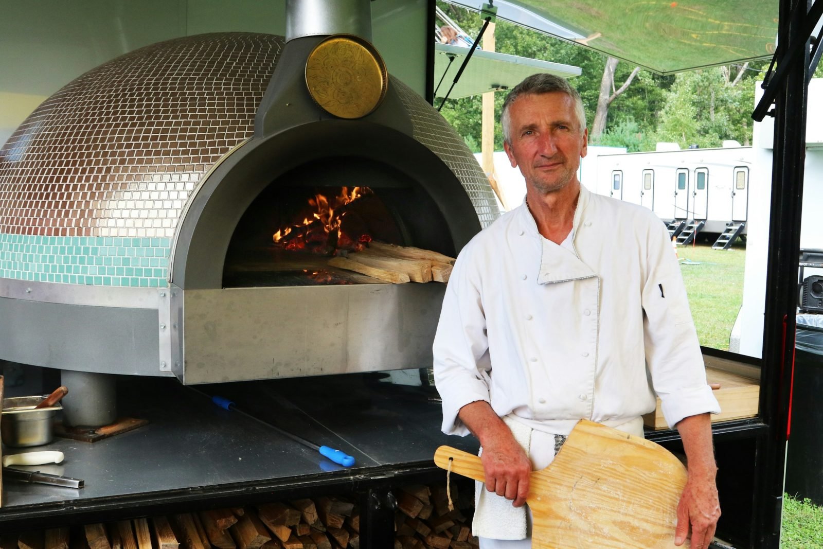 Chef holding a peel beside a tiled wood-fired pizza oven