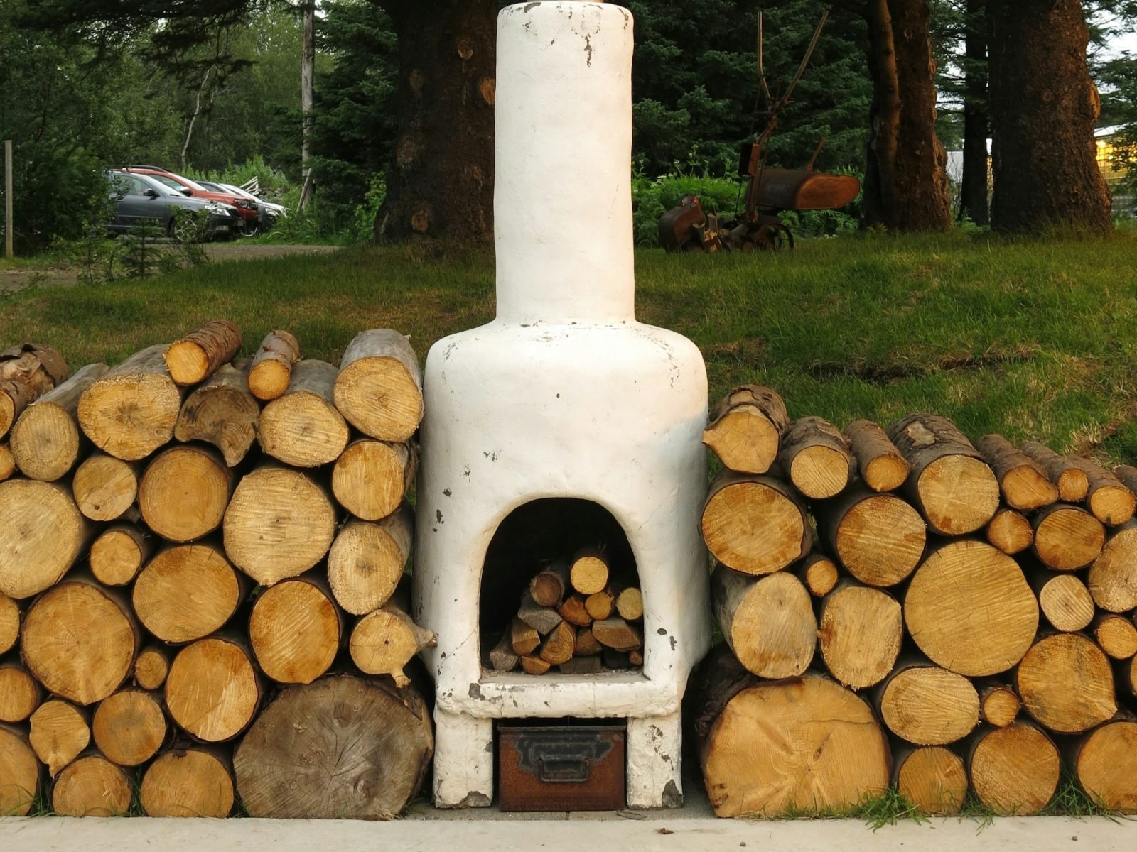 White chiminea with a tall chimney on paving, between neat stacks of split firewood