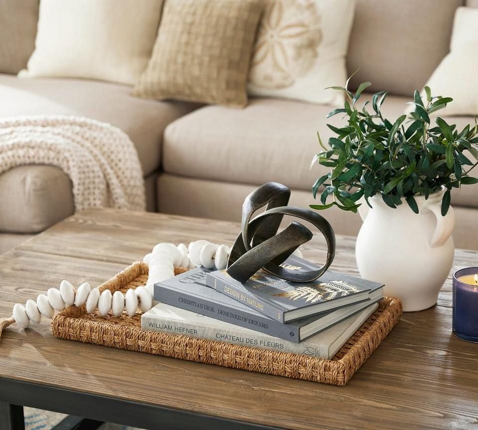 Coffee table styled with a woven tray, books, a sculpture and a vase of greenery