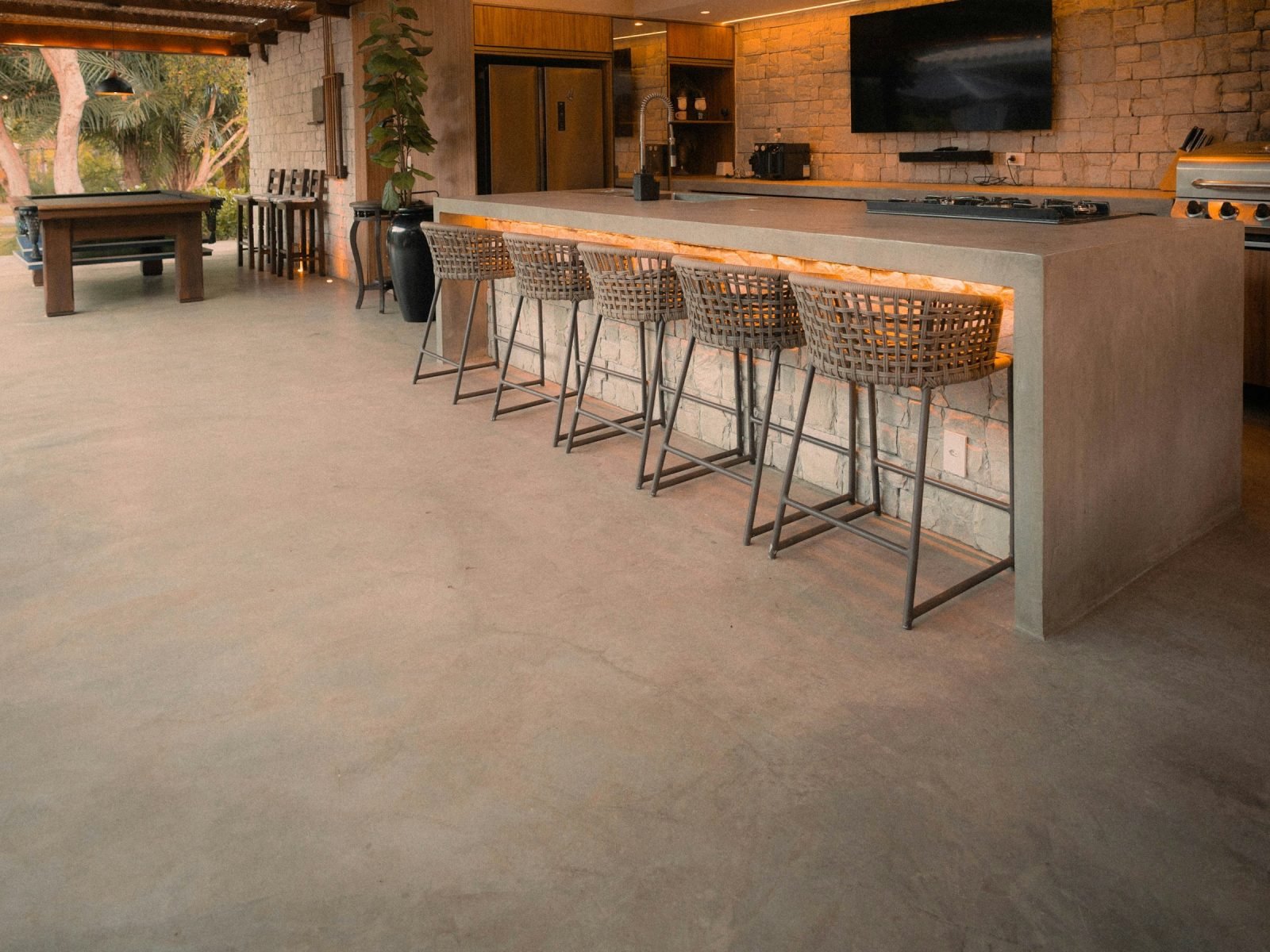 Long polished concrete bar counter with stools under a slatted pergola