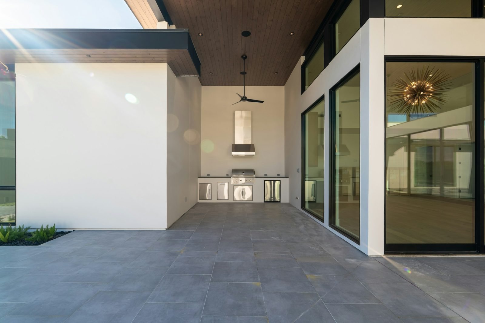 Covered terrace with a built-in outdoor kitchen, stainless grill and a vent hood against a white wall