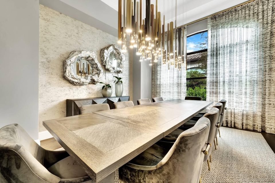 Dining room with sculptural metal mirrors, a brass pendant and patterned sheer curtains