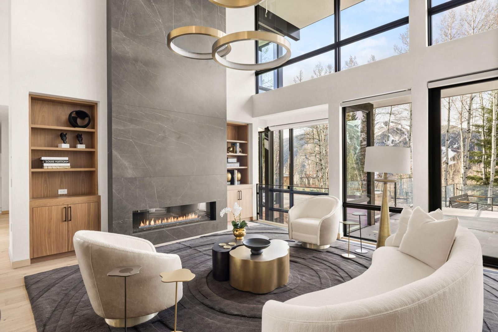 Double-height living room with ring chandeliers, a stone fireplace and curved seating