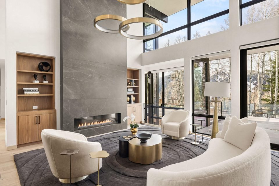 Double-height living room with ring chandeliers, a stone fireplace and curved seating