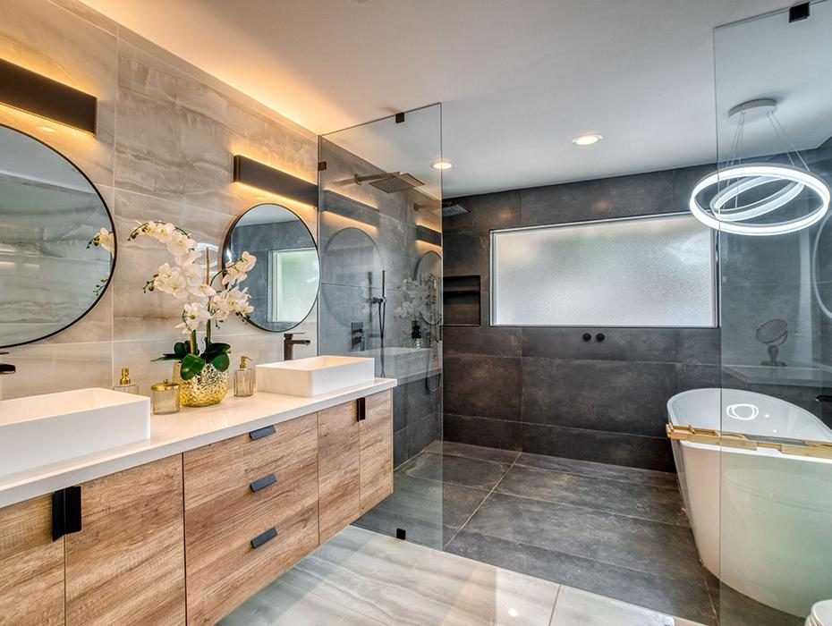 Bathroom with a wood double vanity, round mirrors, walk-in shower and freestanding tub