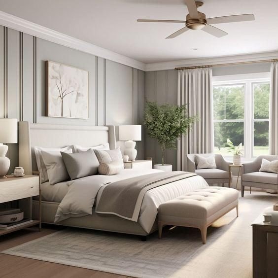 Calm grey bedroom with a panelled wall, upholstered bed, tufted bench, armchairs and a ceiling fan