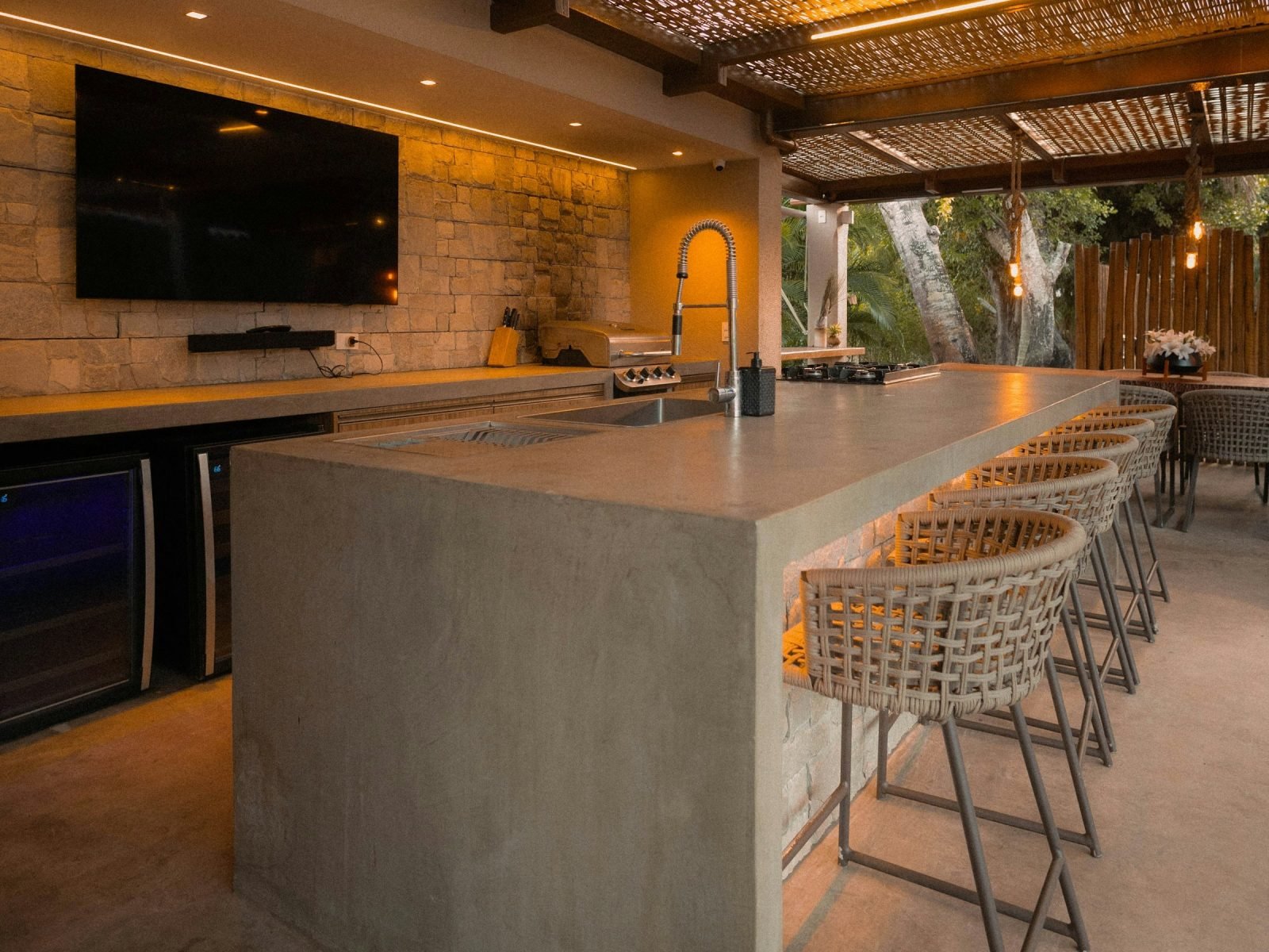 Warm LED strip glowing under a concrete bar counter beside woven stools