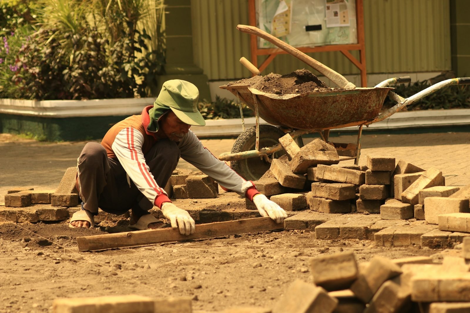 Man laying paving blocks on a levelled bed beside a wheelbarrow