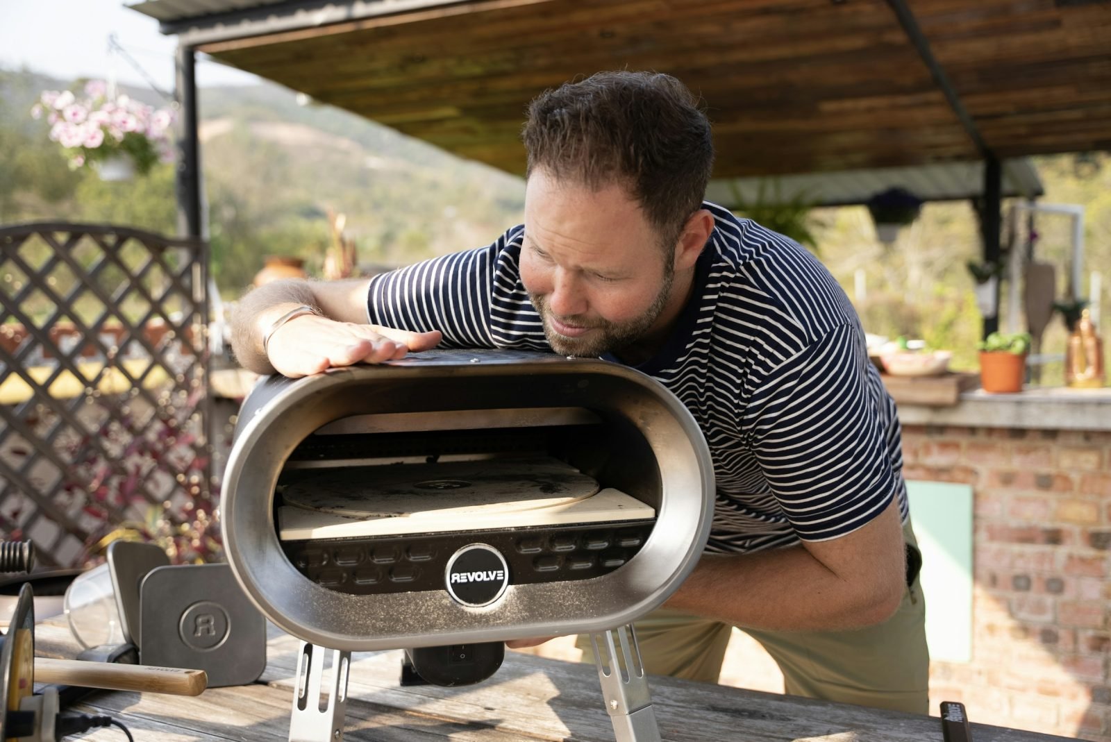 Man checking a compact stainless steel pizza oven set on an outdoor table