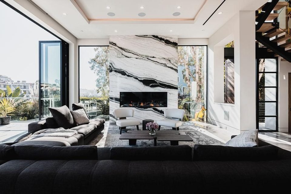Living room with a dramatic marble fireplace wall, black sofa and open glazing
