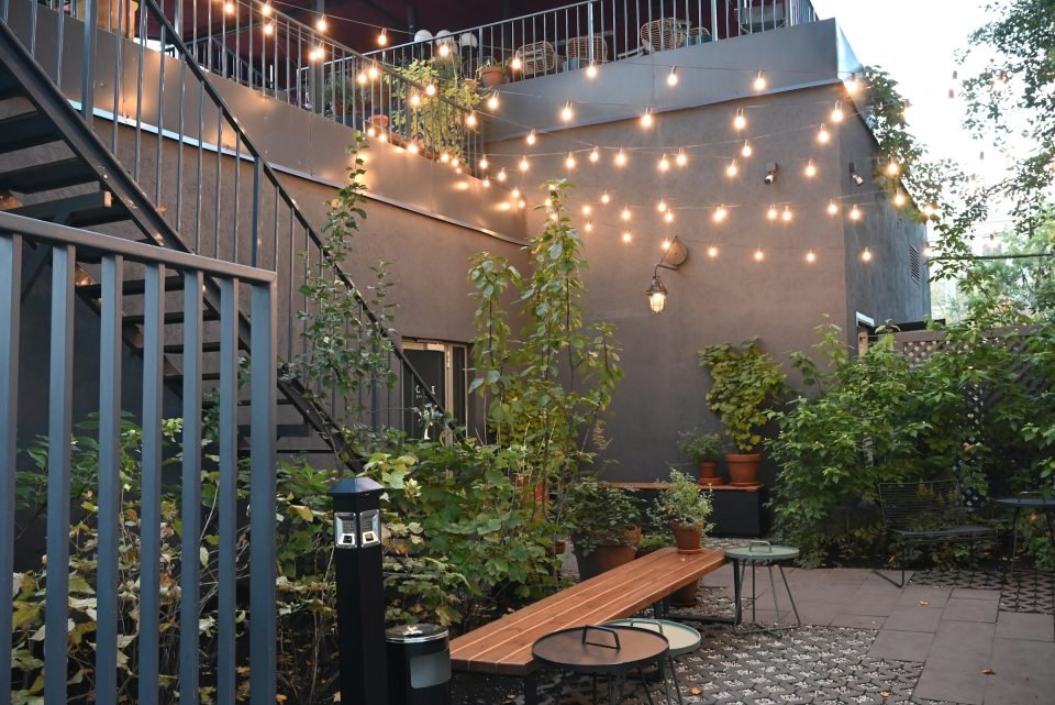 Narrow paved courtyard with string lights, planters and a timber bench at dusk