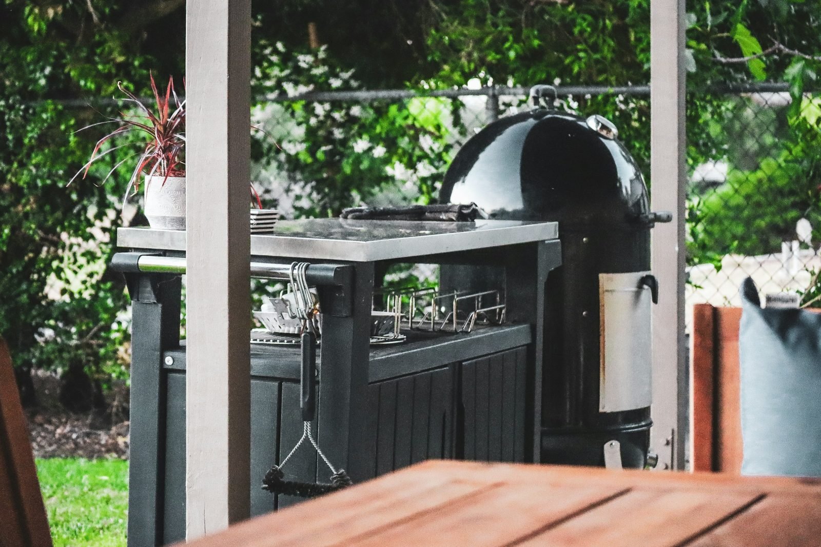 Black kettle grill beside a stainless steel prep station in a planted garden