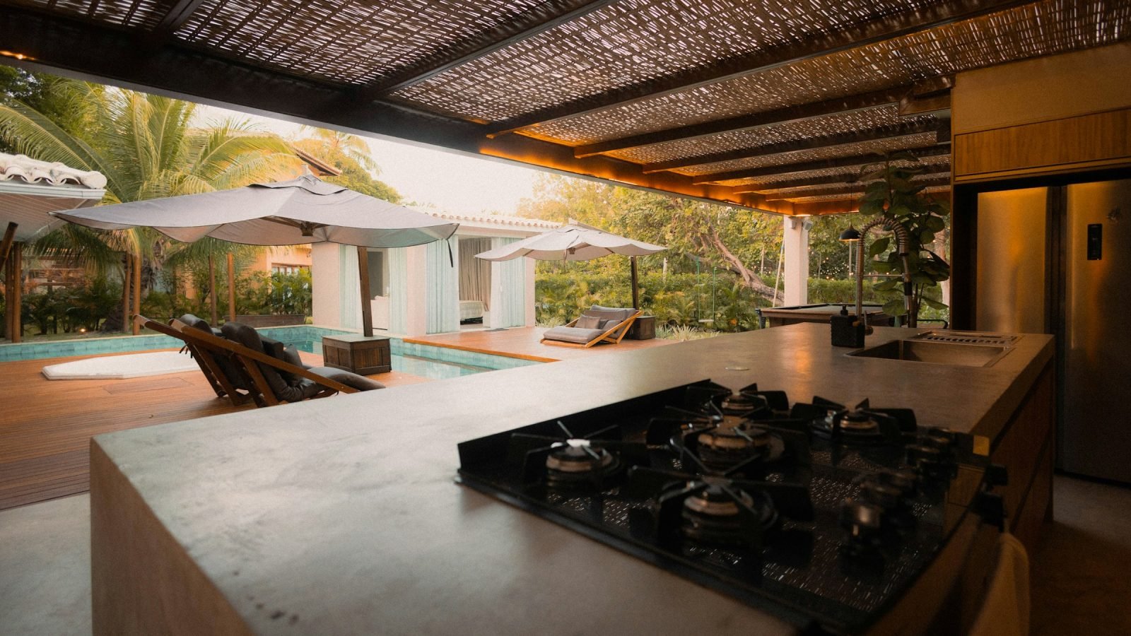 Gas hob set into a concrete outdoor kitchen counter overlooking a pool and sun loungers