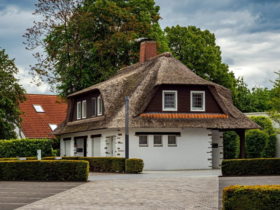 Paved driveway leading to a white house with a thatched roof