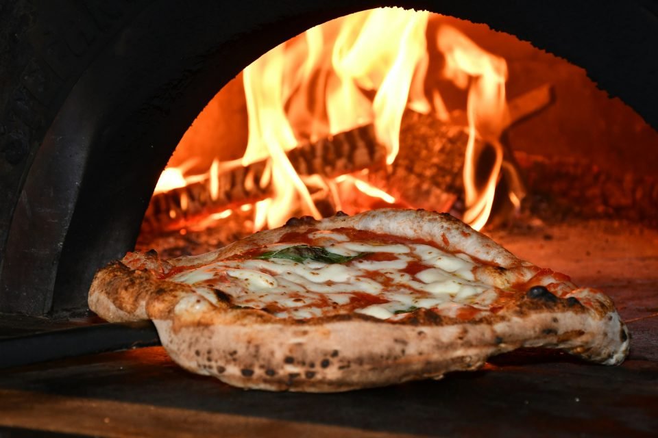 Pizza with a puffed, blistered crust baking beside wood flames