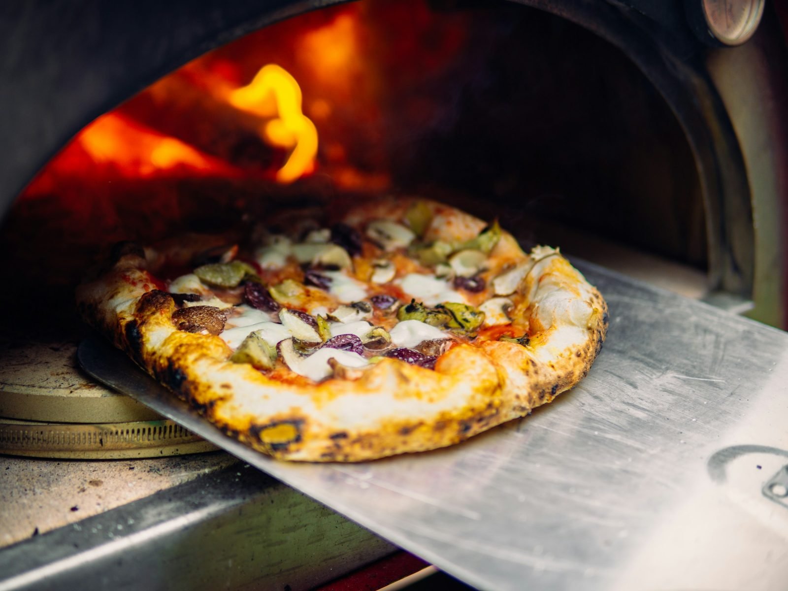 Pizza lifted out of a wood-fired oven on a metal peel