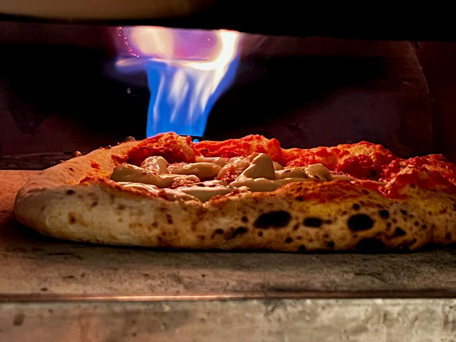 Pizza cooking under the blue flame of a gas oven