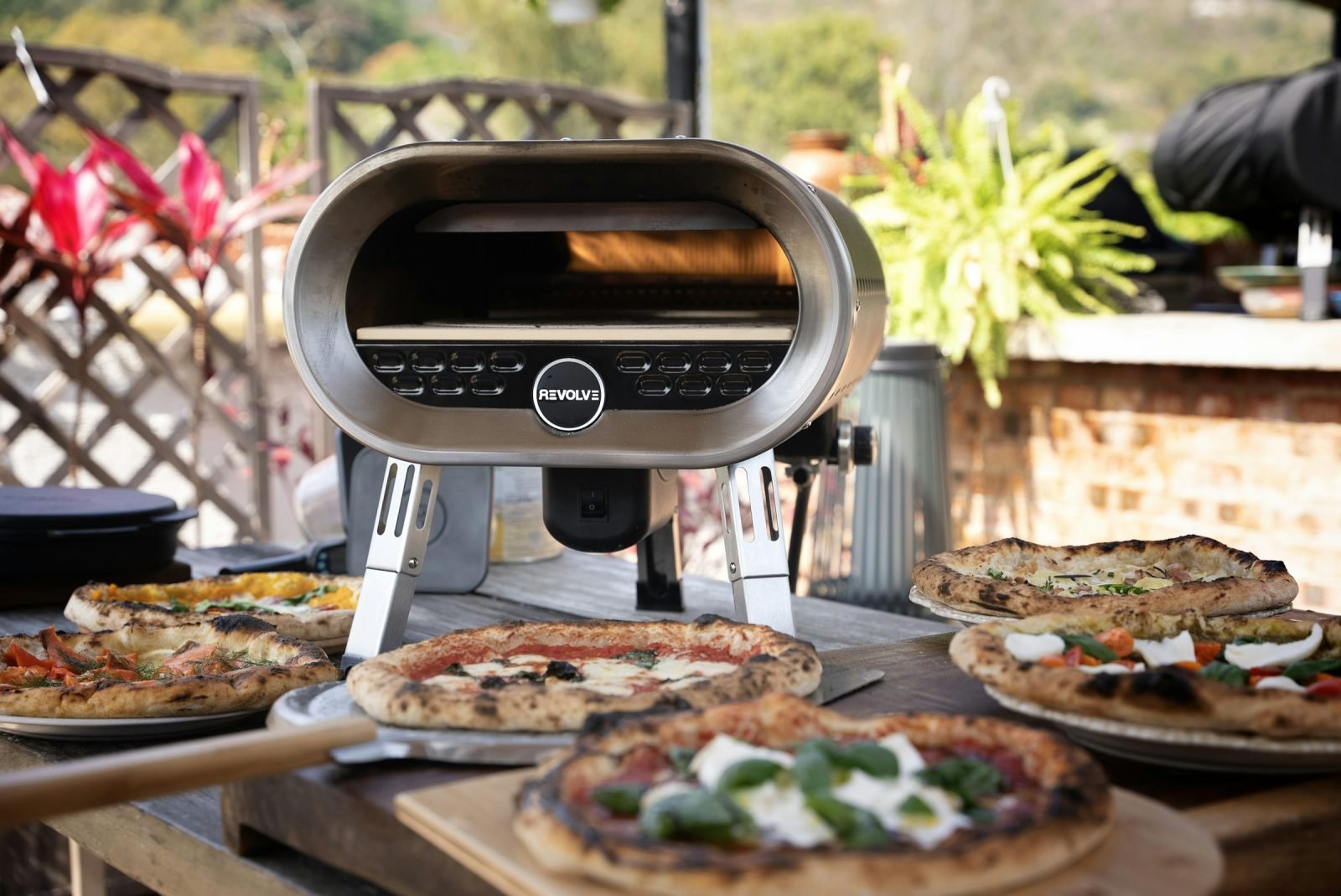 Table of fresh pizzas laid out beside an outdoor oven