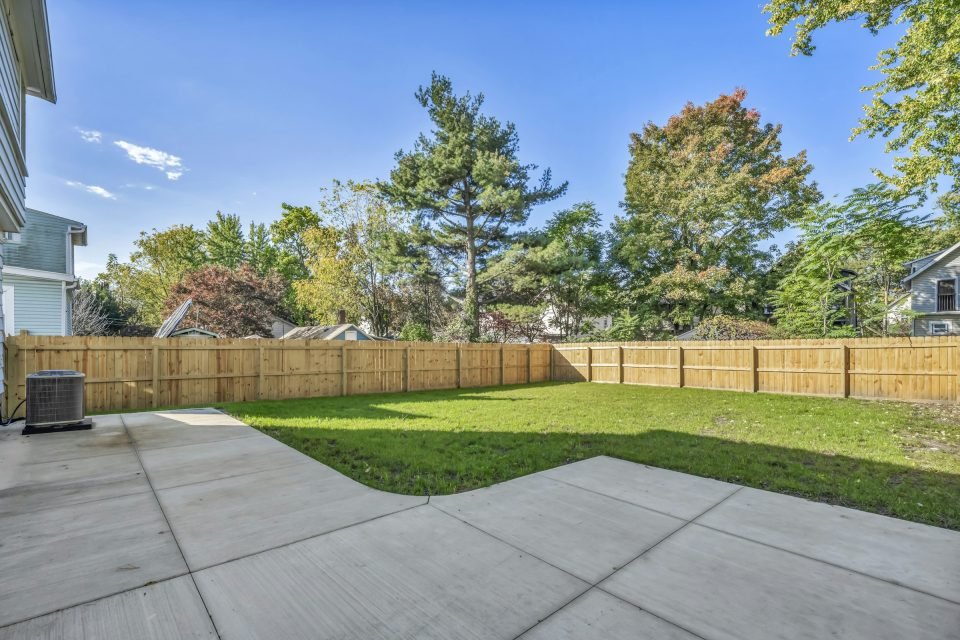 Small lawned garden and patio enclosed by a tall wooden fence