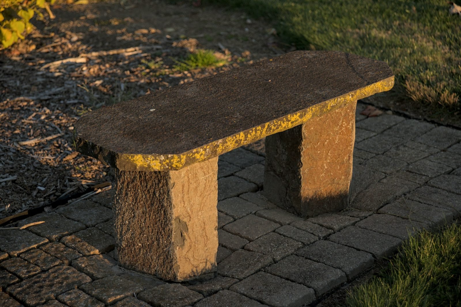 Stone slab bench on block paving in low sunlight