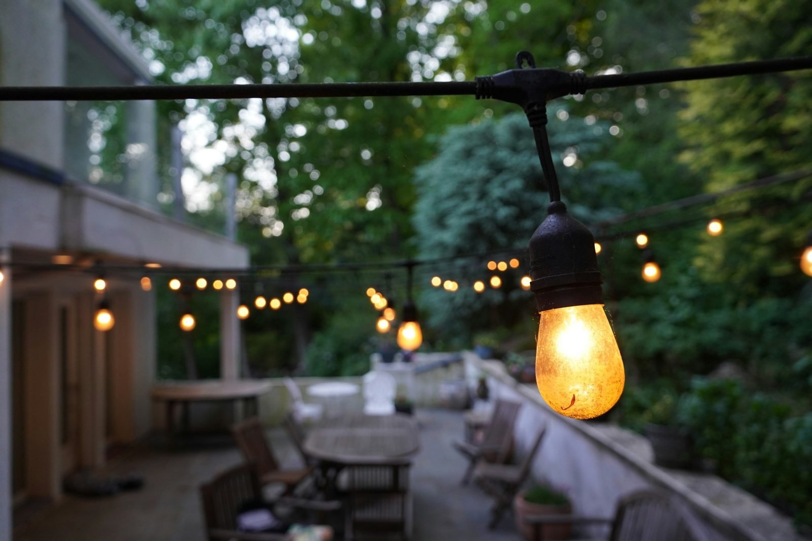 Festoon string lights glowing over a patio with tables and chairs