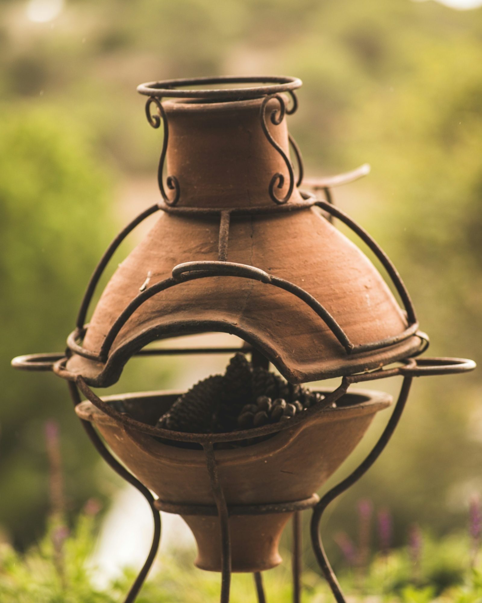 Traditional terracotta chiminea held in a wrought iron stand in a green garden