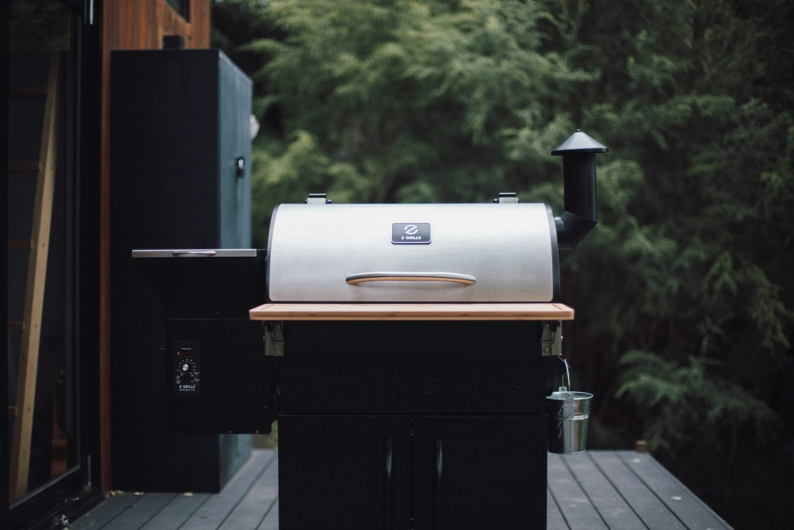 Black pellet cooker on a wheeled cart with a chimney, on a small deck
