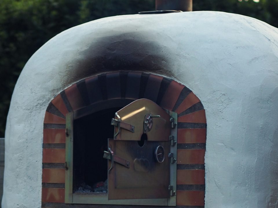 White rendered dome pizza oven with a brick arch in a garden