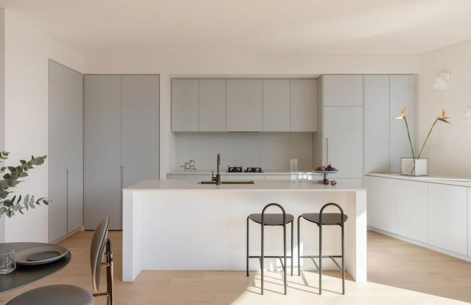 Minimal white kitchen with an island, black bar stools and handleless grey cabinetry