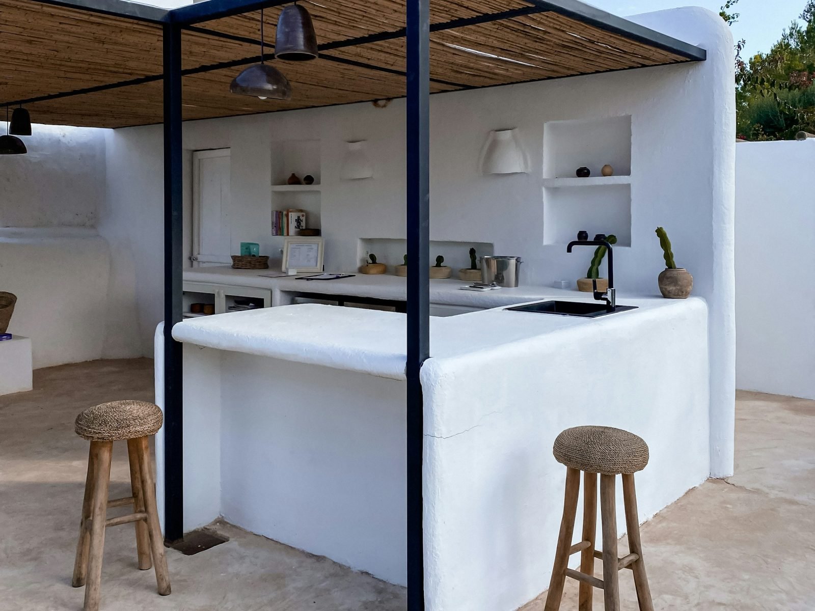 White rendered outdoor kitchen with a counter, shelving and wooden stools